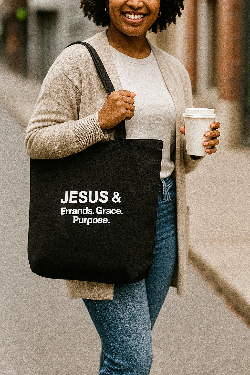 Person holding a black tote bag with text and a coffee cup on a city street.
