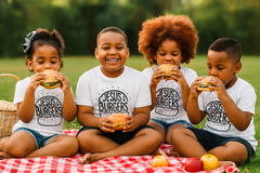 Four children sitting on a blanket outdoors, eating burgers with 'Jesus Burgers' shirts.
