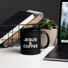 Black mug with 'JESUS & COFFEE' text on a desk with laptop, books, and plant.