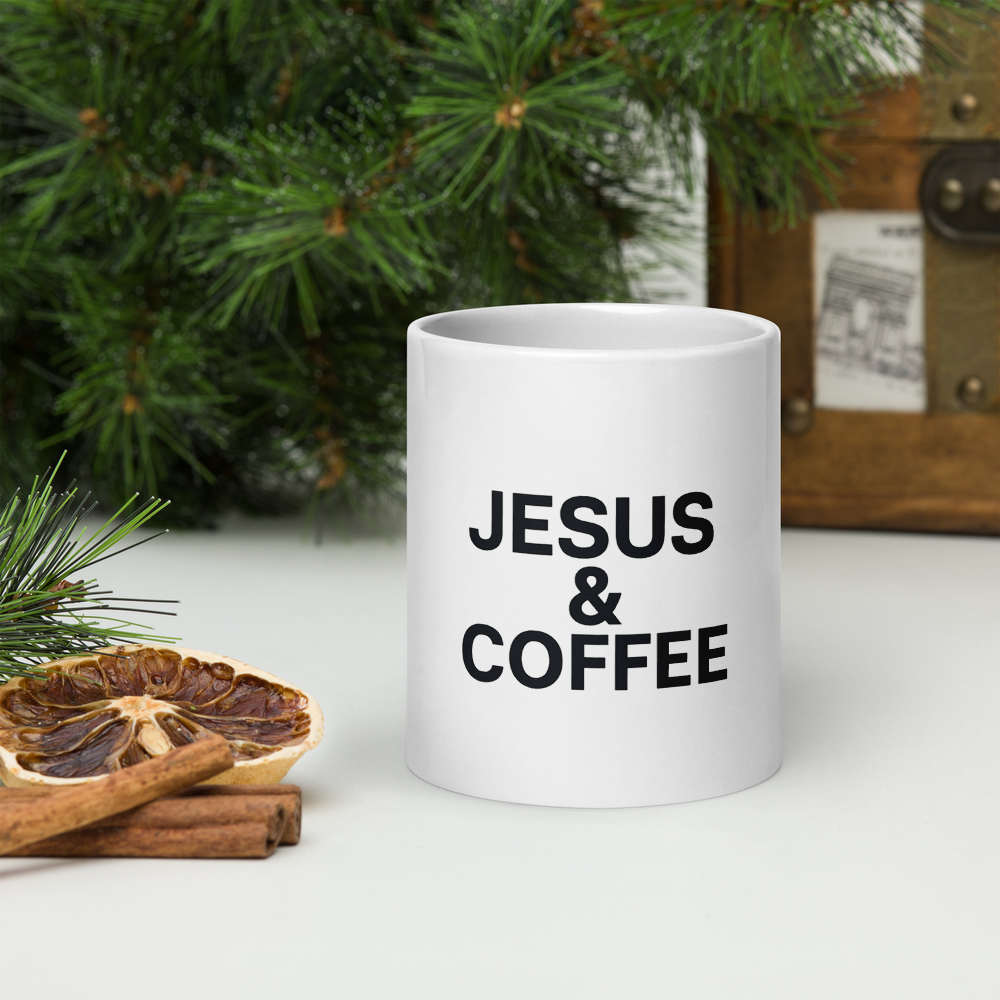 White mug with 'JESUS & COFFEE' text on a surface with Christmas decorations.